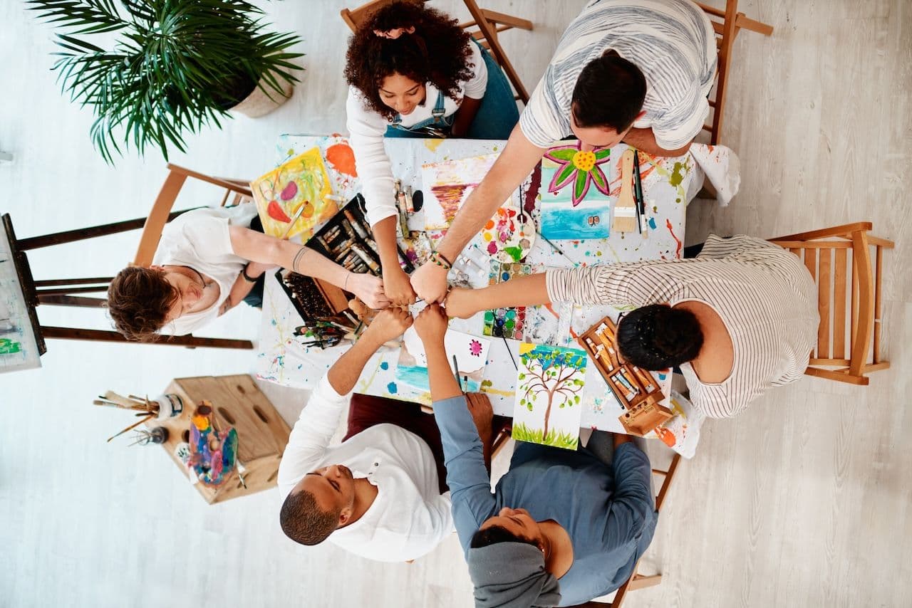 retreat theme idea: group of people sitting around a art table, fist bumping 