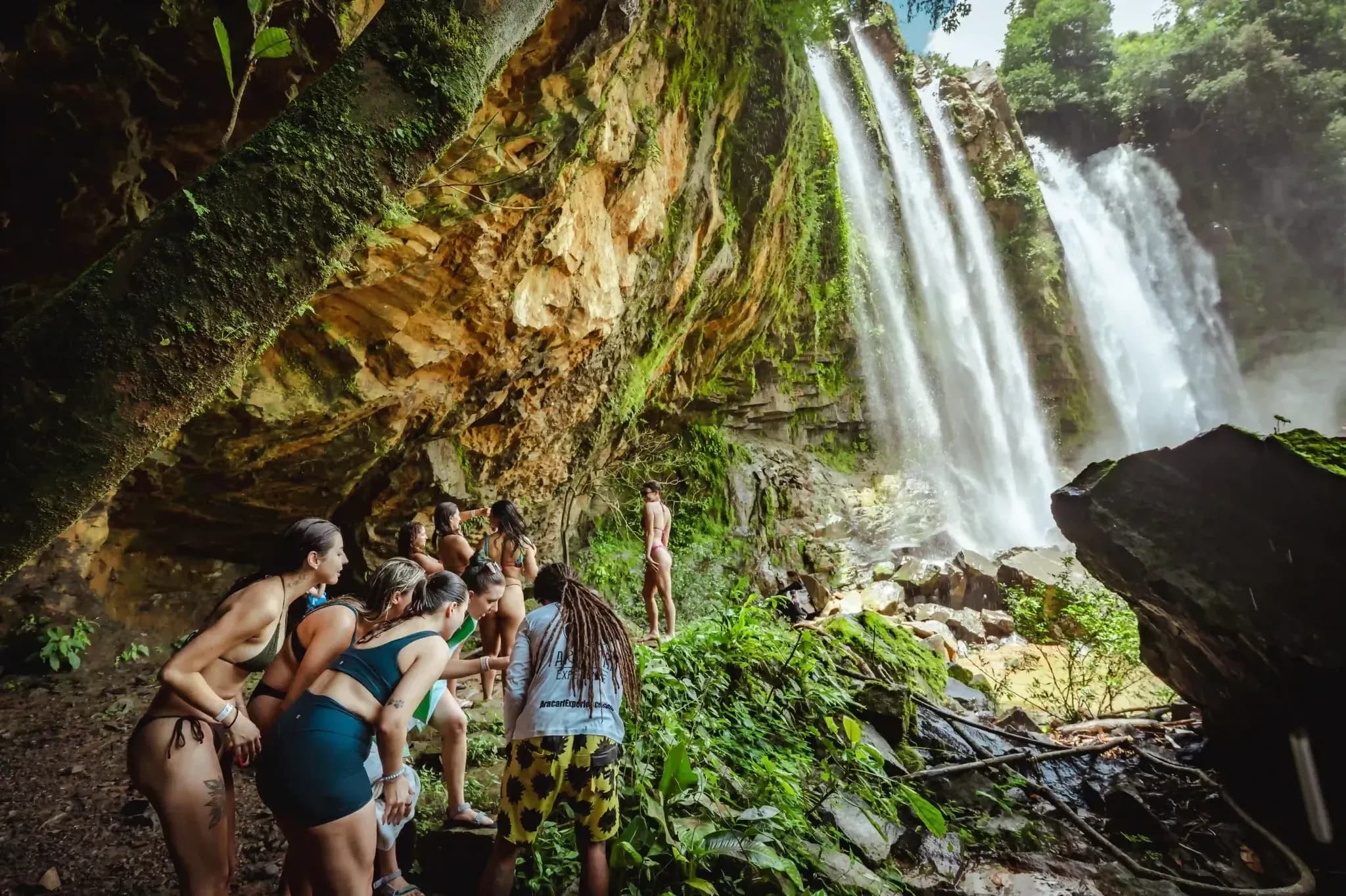 Guests from Vajra Jahra Retreat Center exploring behind a majestic tropical waterfall surrounded by lush greenery.