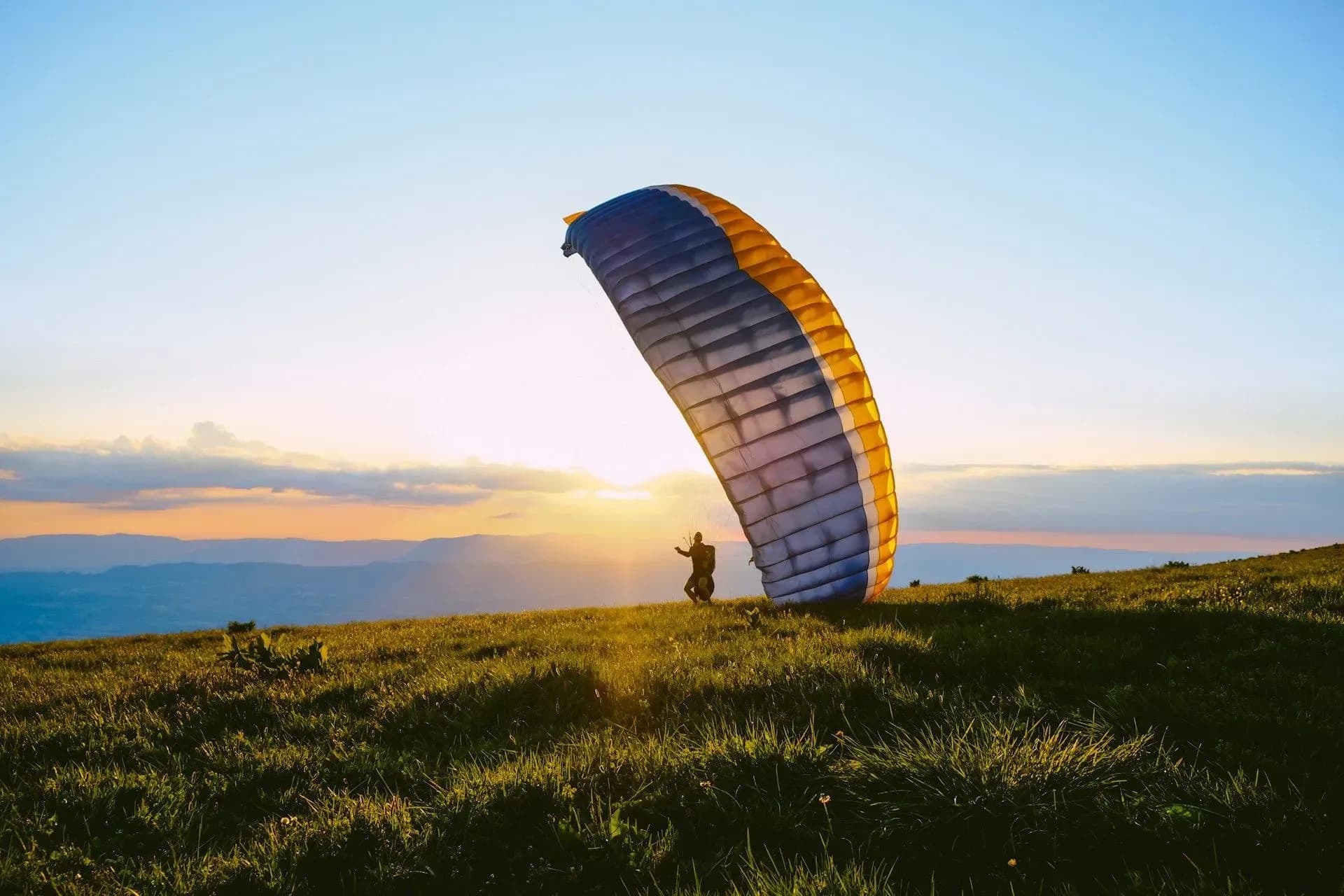 Person preparing to paraglide at sunrise over a grassy hill, showcasing adventure opportunities available near Vajra Jahra Retreat Center during Costa Rica Yoga Teacher Training.