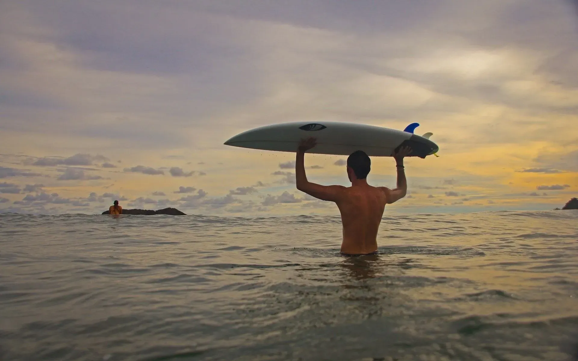 A guest wades into the ocean with a surfboard during sunset near Vajra Jahra Retreat Center, an unforgettable setting that stands out among Costa Rica wedding venues.