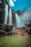 Group of people swimming beneath the twin Diamante Waterfalls in Costa Rica, surrounded by lush jungle cliffs and mist.